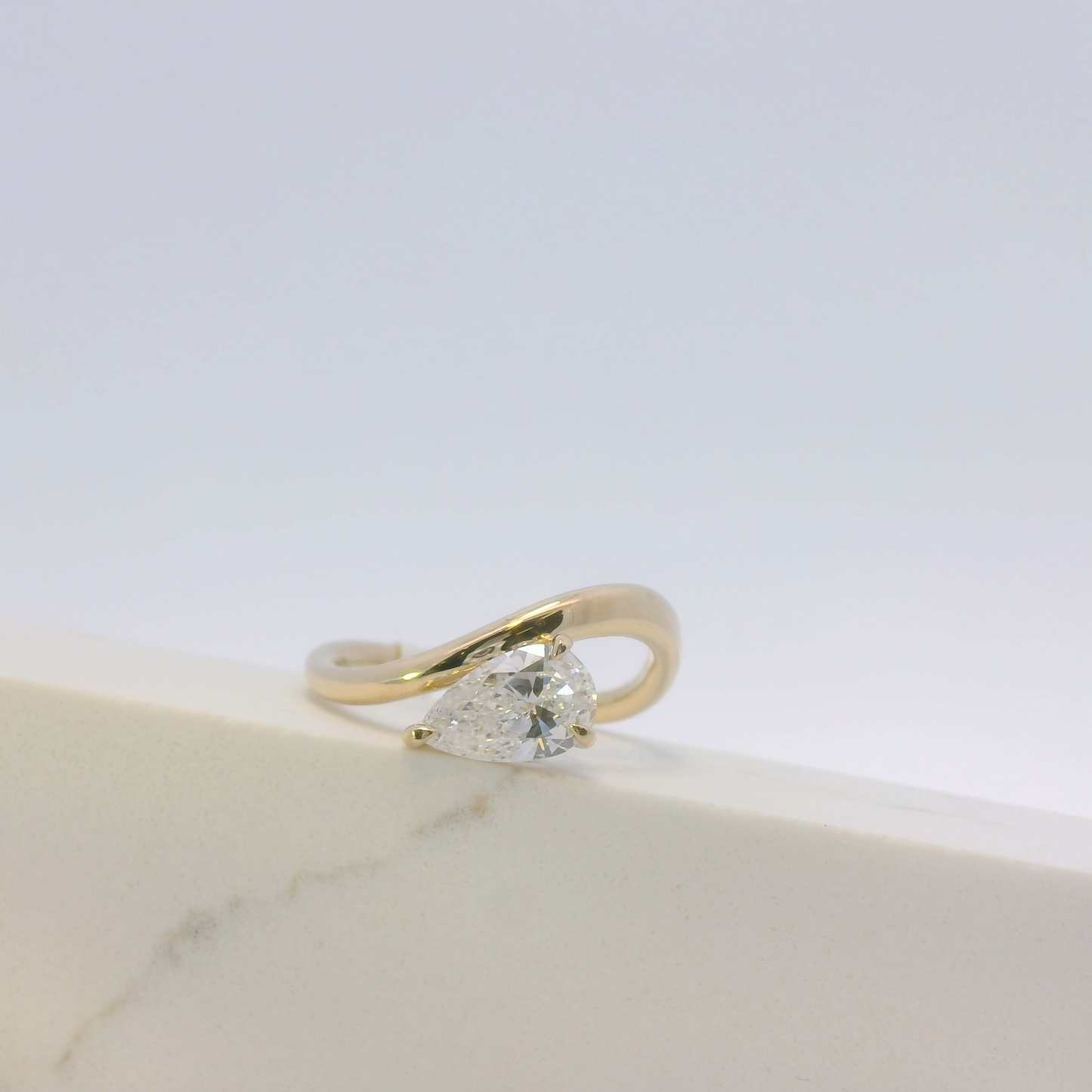 Gold ring with a pear-shaped diamond on a light background