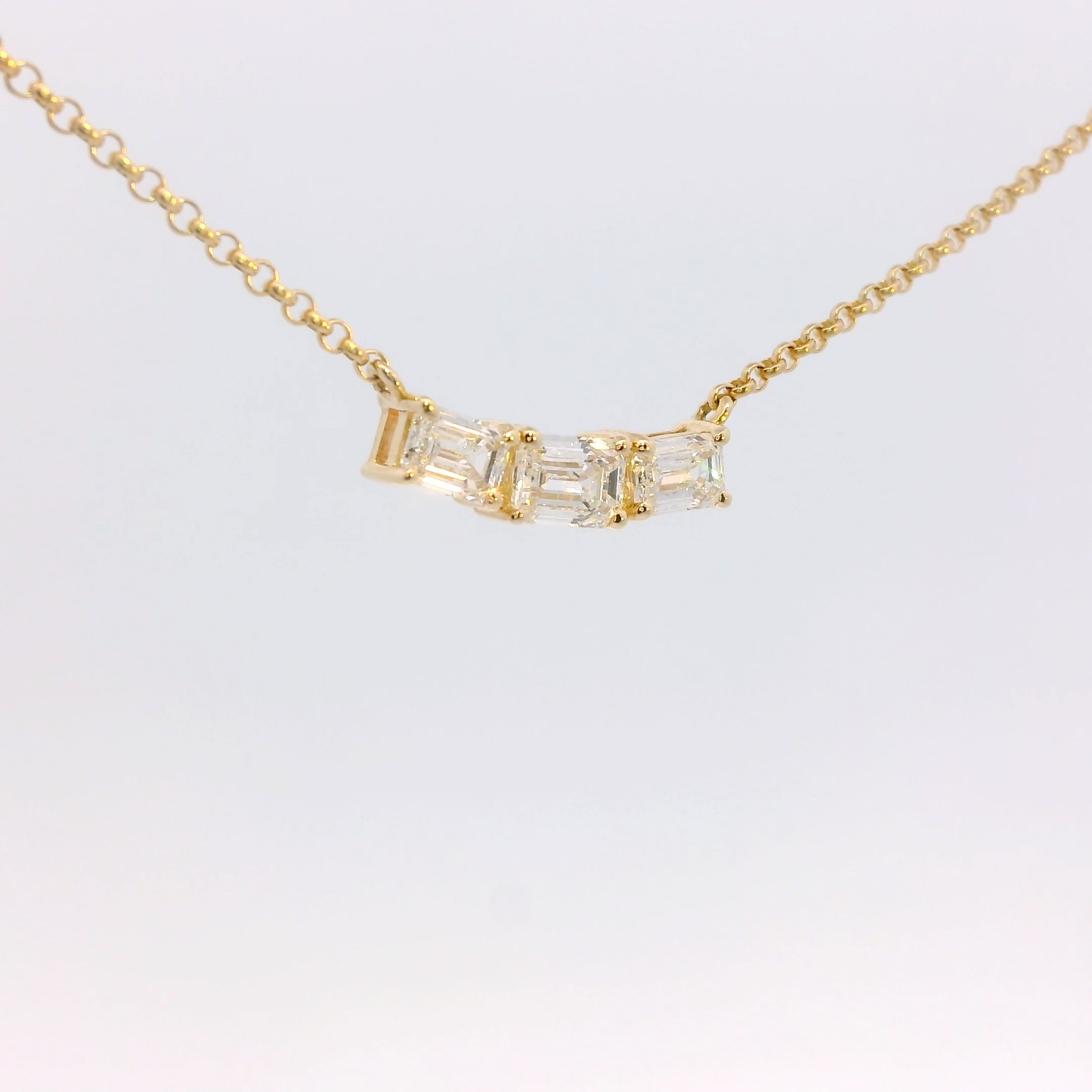 Gold necklace with a baguette-cut diamond pendant on a light gray background