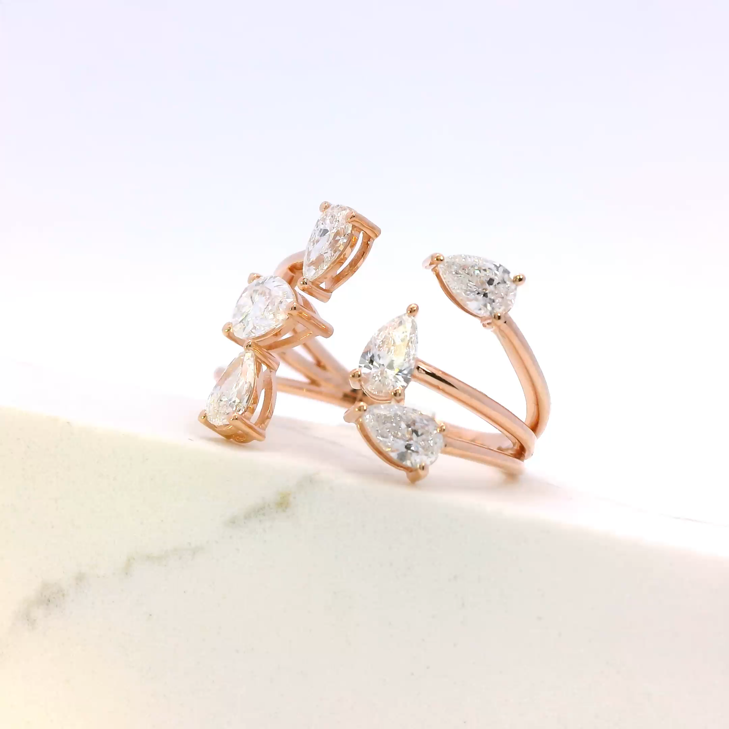 Rose gold ring with pear-shaped diamonds on a marble surface