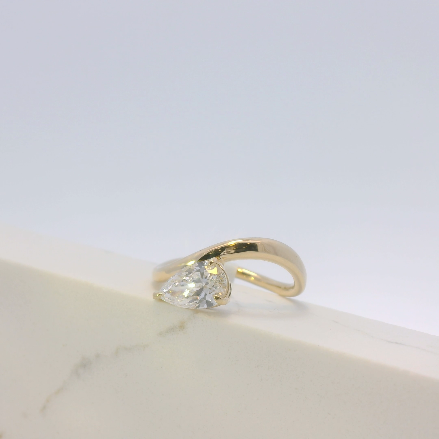 Gold ring with a clear gemstone on a light marble surface