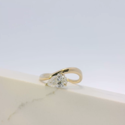 Gold ring with a pear-shaped diamond on a light background